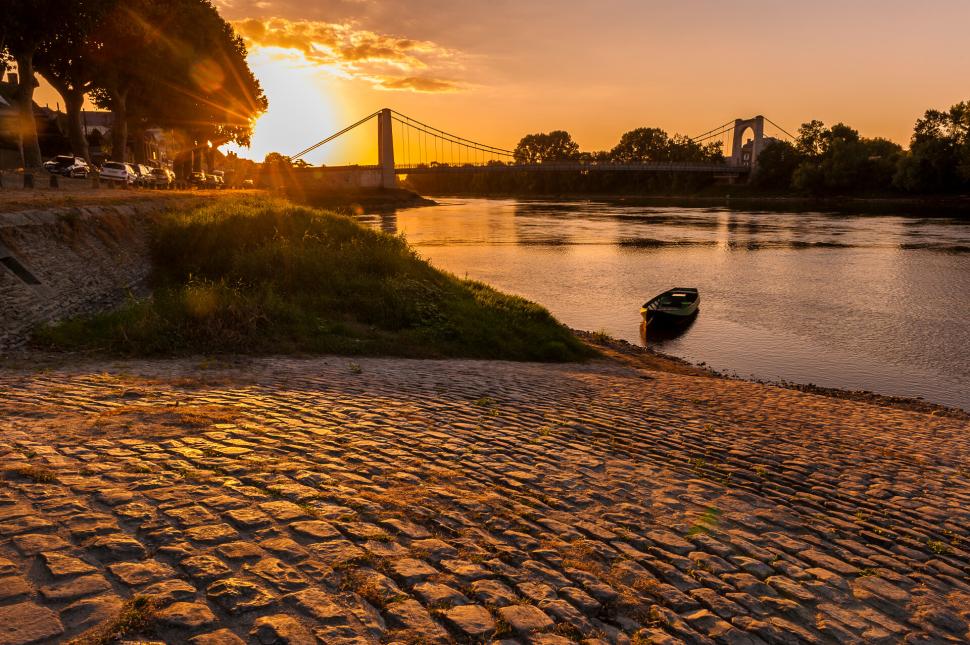 Vue sur la Loire et le pont, depuis les quais. Le soleil se couche juste derrière le pont, au dernier plan.