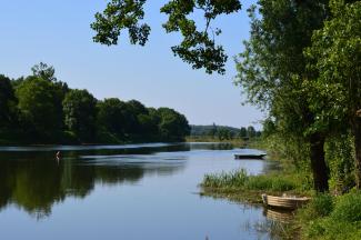 Bords de la Sarthe par beau temps, avec deux barques amarrées au premier plan parmi roseaux et arbres verdoyants.