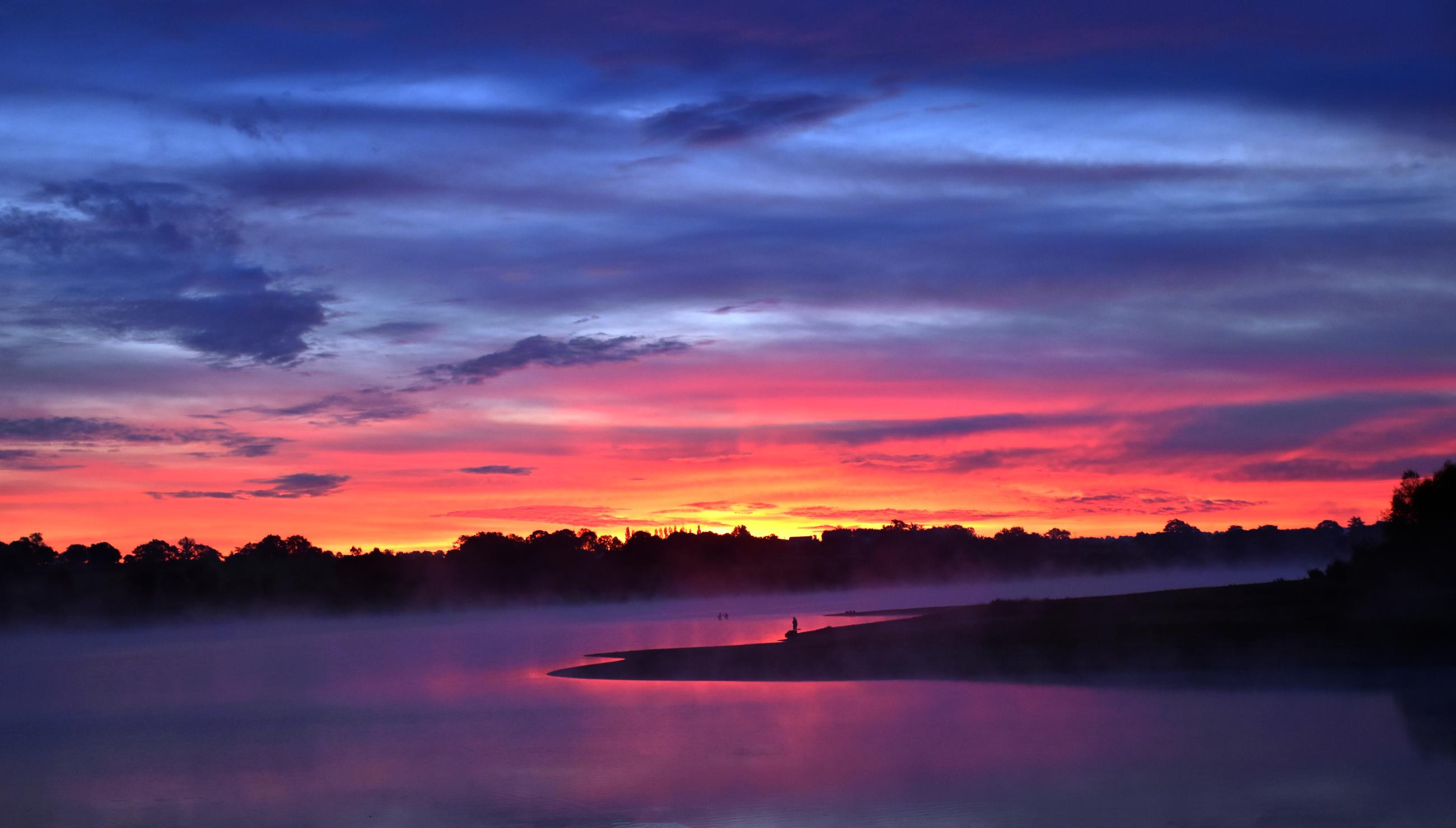 Reflets roses et nuages bleutés sur le lac du Verdon. Au lointain les dernières lueurs du soleil et devant, une silhouette sur une langue de terre., 